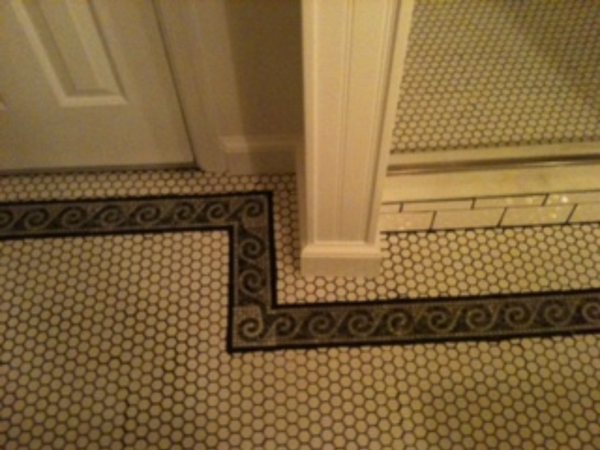 White hexagon floor tile with a black Greek-key border wrapping around a trimmed column