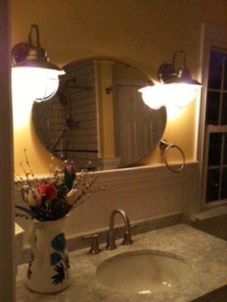Oval mirror between two nickel sconces above a marble vanity top