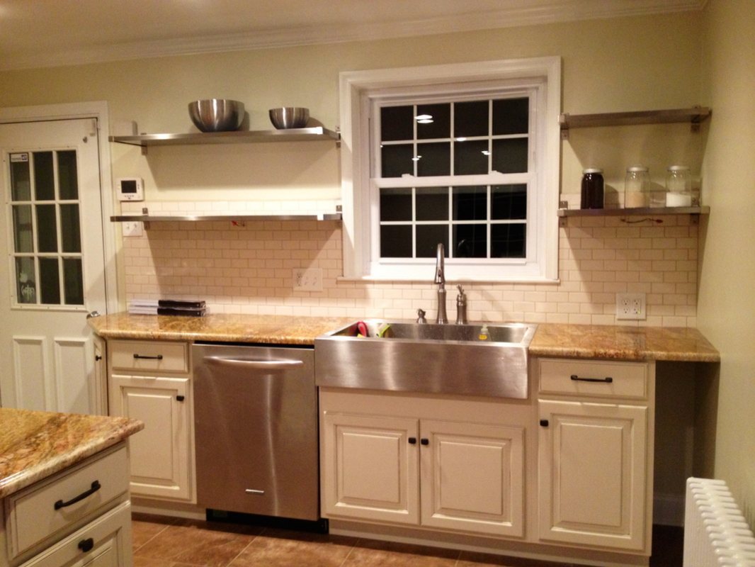Sink wall with a stainless farmhouse sink, open steel shelves and bisque subway tile