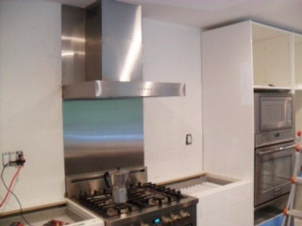 In progress: stainless range hood and backsplash panel over a gas range