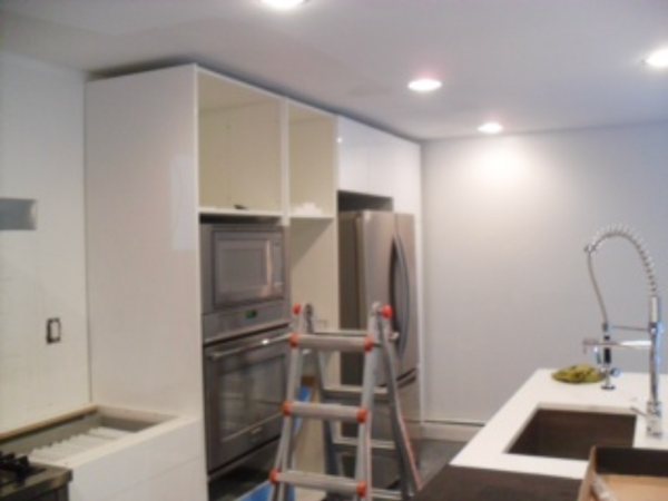 In progress: tall white gloss cabinets with built-in wall ovens and refrigerator