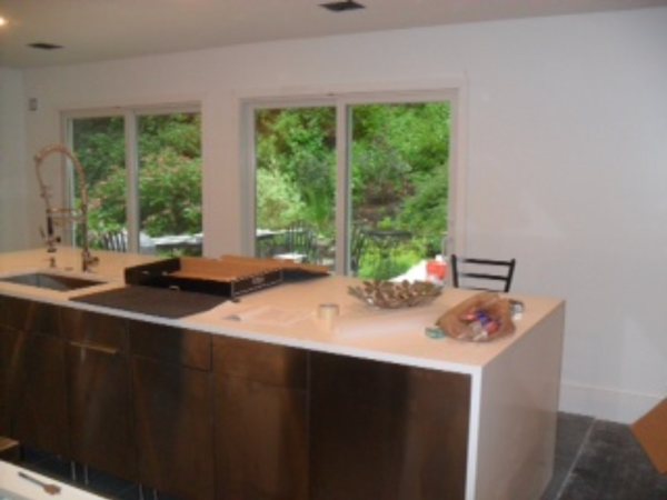 In progress: white waterfall-edge island with dark wood cabinets in front of large windows